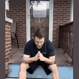 a man is squatting down on a yoga mat in front of a brick building .