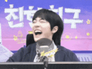 a man is laughing while sitting in front of a microphone with chinese writing in the background .