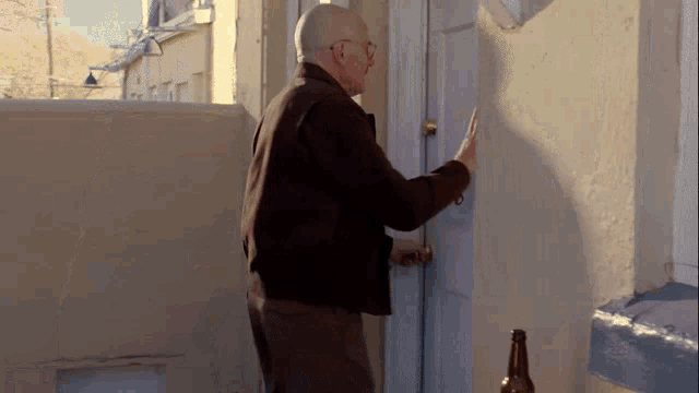 a man is standing in front of a door with a bottle of beer .