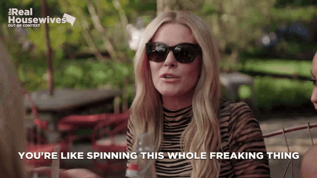 a woman wearing sunglasses says " you 're like spinning this whole freaking thing " while sitting at a table