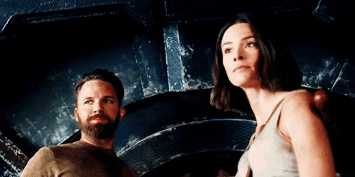 a man with a beard and a woman in a tank top are standing next to each other in a dark room .
