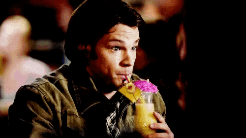 a man in a brown jacket is holding a drink with a flower in it