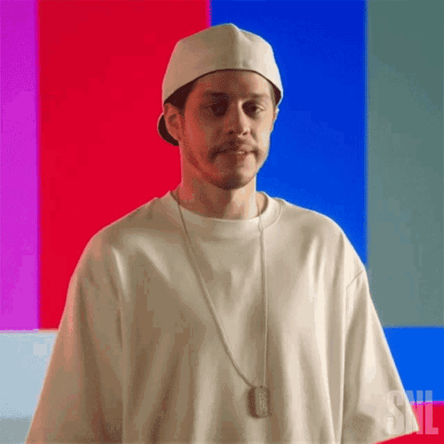 a man wearing a hat and a necklace is standing in front of a colorful background with the letter s on it .
