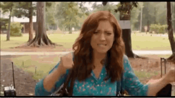 a woman with red hair and a blue shirt is sitting in a park with trees in the background .