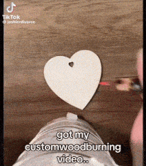 a person is making a heart with a hole in it and says " got my custom woodburning video "