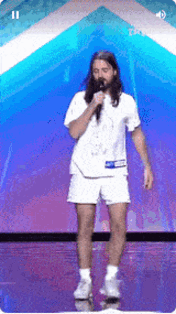 a man with long hair and a beard is singing into a microphone on a stage