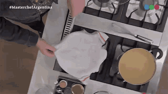 a person covering a pan with a towel on a stove with the hashtag #masterchefargentina