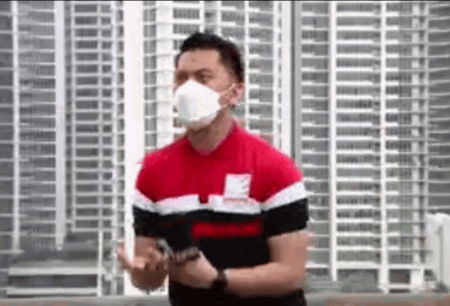 a man wearing a face mask and a red shirt is standing in front of a tall building .
