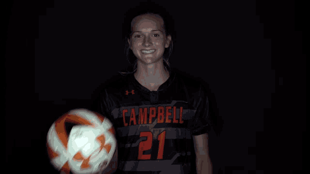 a girl wearing a campbell 21 jersey holds a soccer ball