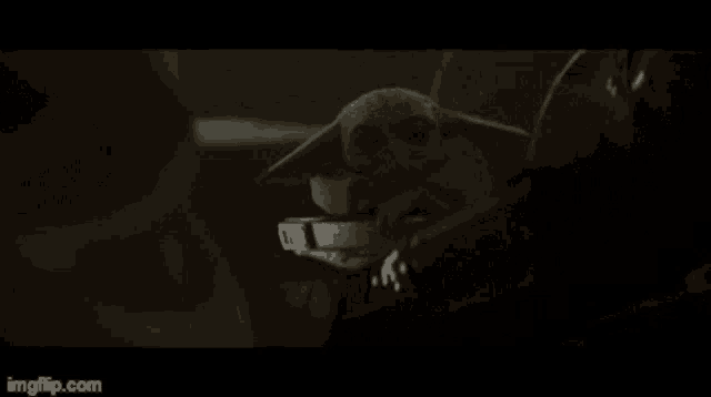 a baby yoda is sitting on top of a metal object in a dark room .