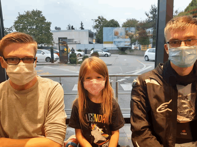 a girl wearing a shirt that says legend sits between two men wearing masks