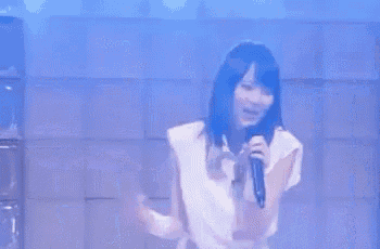 a woman is singing into a microphone with her arms outstretched in front of a blue wall .