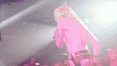 a woman in a pink shirt is singing into a microphone on stage