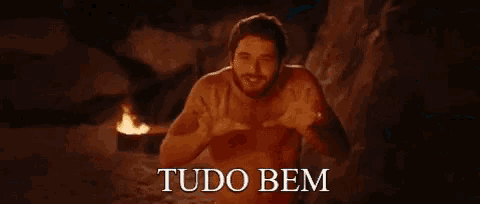 a shirtless man is standing in front of a fire with the words tudo bem written below him