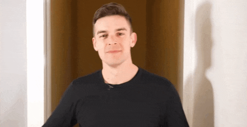 a man in a black t-shirt is standing in a doorway and smiling .