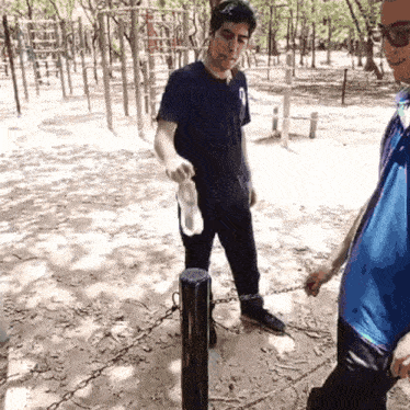 a man in a blue shirt holds a bottle of water while standing next to another man