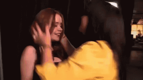 a woman covering her ears with her hands while a man in a yellow jacket holds her head .