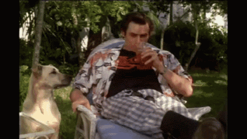 a man is sitting in a chair with a dog while drinking a drink .