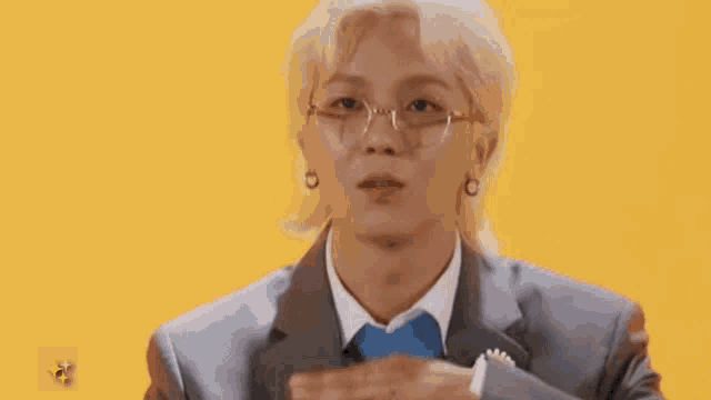 a man wearing glasses and a suit is making a heart shape with his hands .