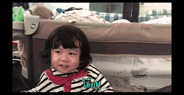 a little girl in a striped shirt is sitting in a crib and says " oi "