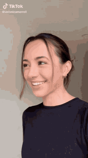 a woman wearing a black shirt and earrings is smiling for a tiktok video .