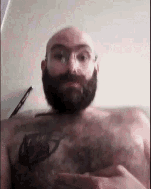 a bald man with a beard and tattoos on his chest is taking a selfie .