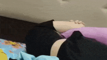 a person is laying on a bed with a purple pillow and a black shirt on .