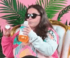 a woman wearing sunglasses is sitting in a chair holding a bottle and a pill .