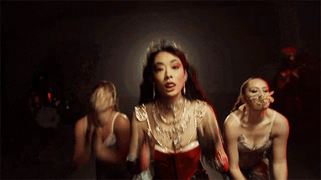 a woman in a red corset is surrounded by two other women in white lingerie .