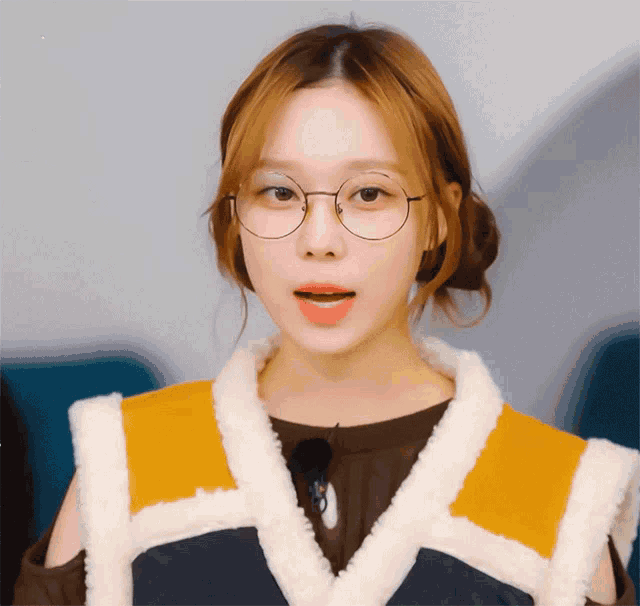 a woman wearing glasses and a furry vest looks at the camera