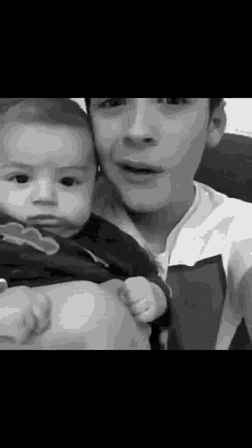 a man is holding a baby in his arms and the baby is looking at the camera .