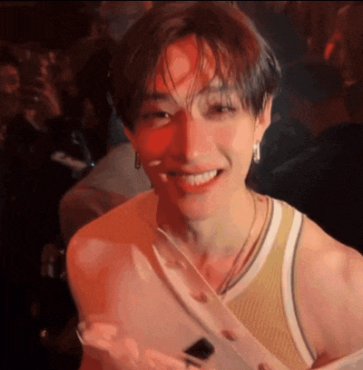 a young man in a tank top is smiling and looking at the camera in a crowded room .