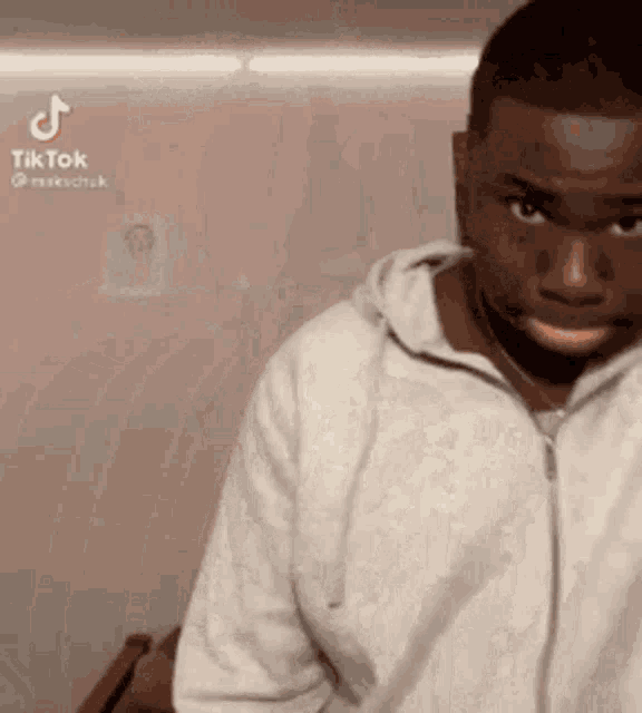 a man in a white hoodie is making a funny face while standing in front of a wall .