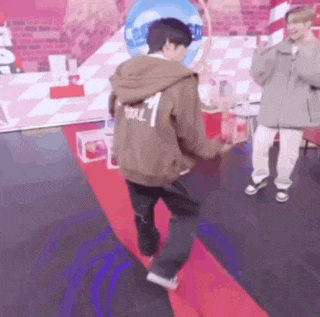a man in a brown hoodie is dancing on a red carpet while another man looks on .