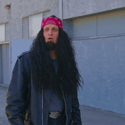 a man with long hair and a beard wears a red bandana