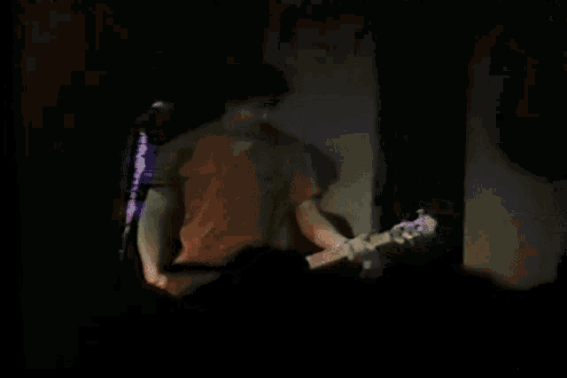 a man in a red shirt is playing a guitar in front of a microphone