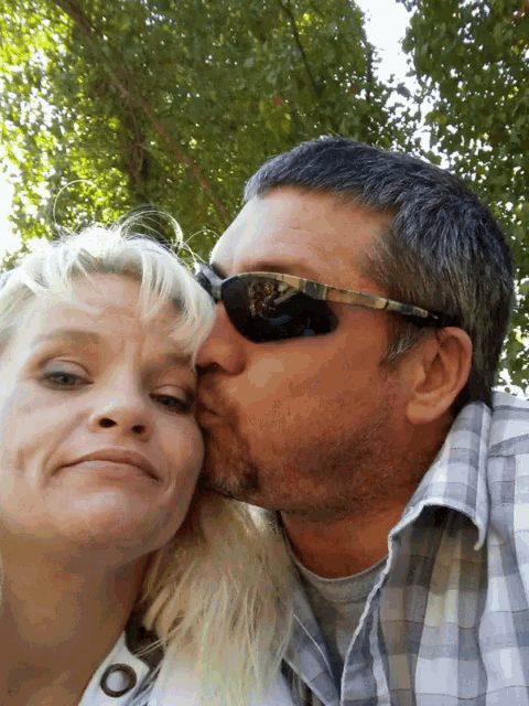 a man is kissing a woman on the cheek while wearing sunglasses