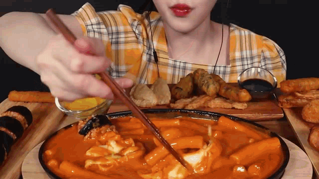 a woman in a plaid shirt is holding chopsticks over a bowl of sauce