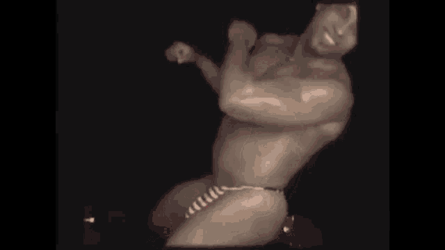 a shirtless man wearing a red hat is standing in a dark room .