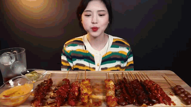 a woman in a colorful sweater is eating a variety of skewers