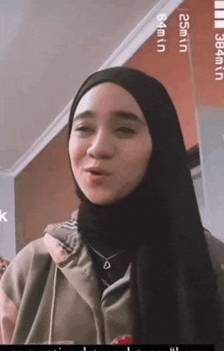 a woman wearing a hijab and a necklace is standing in front of a sign that says 25min