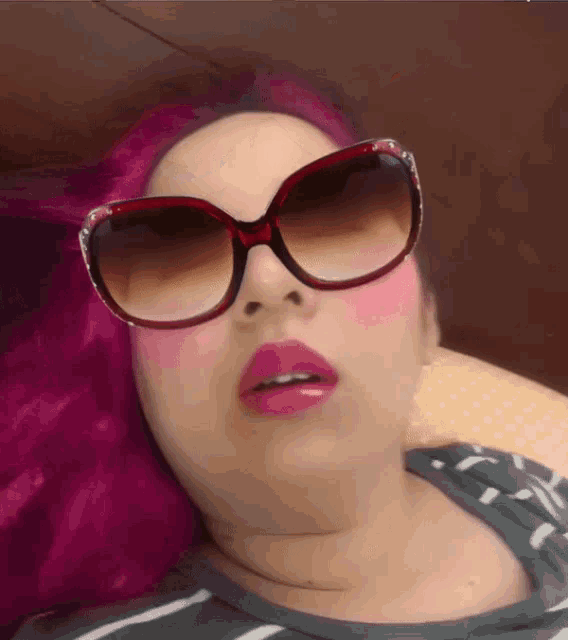 a woman with pink hair wearing red sunglasses