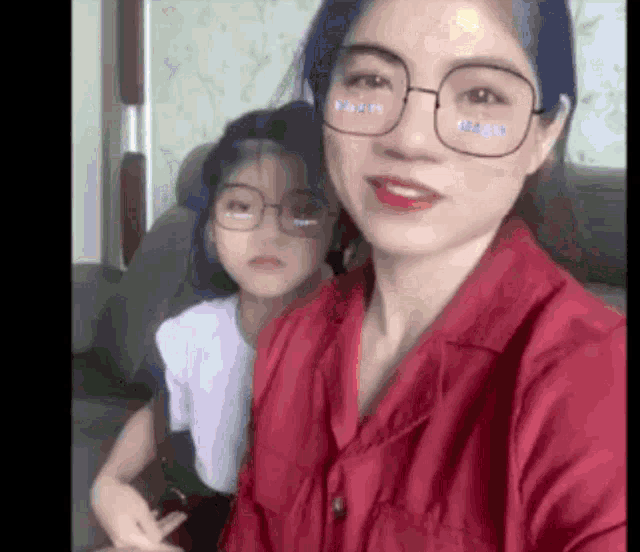 a woman wearing glasses and a red shirt is sitting next to a little girl with blue hair .