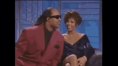 a man in a red suit and sunglasses is sitting next to a woman in a purple dress .