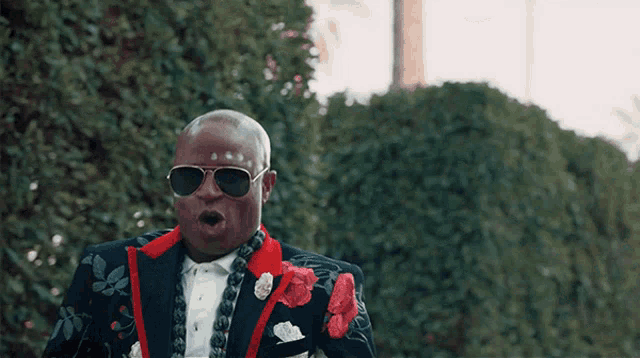a bald man wearing sunglasses and a suit with red flowers on it
