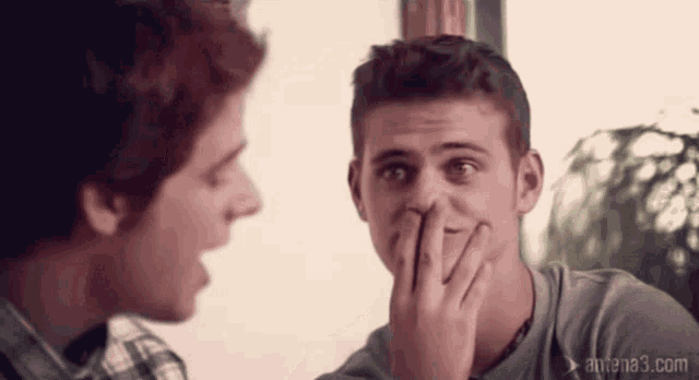 a man covering his mouth with his hand while another man laughs with antena3.com written on the bottom