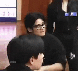 a man wearing glasses is sitting at a table with a woman standing behind him .