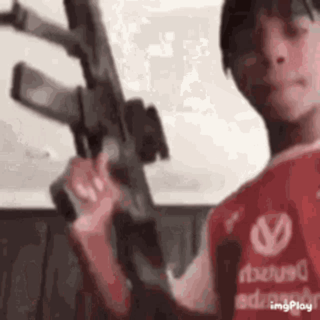 a man in a red shirt is holding an assault rifle .