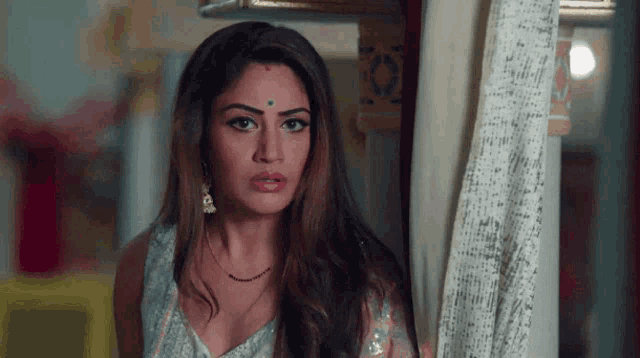 a woman with a bindi on her forehead is standing in front of a window .