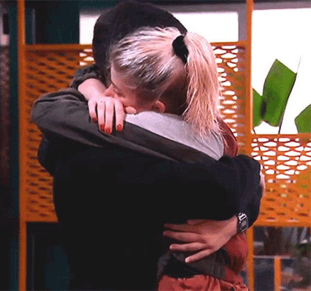 a woman with red nails is hugging a man in front of a yellow wall